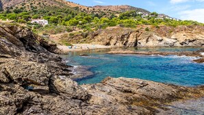 Paesaggio costiero con terreno roccioso, acqua blu cristallina e edifici su una collina.