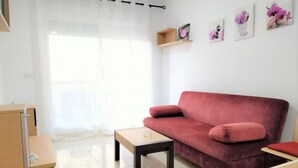 Ein modernes Wohnzimmer mit einem roten Sofa, einem Holztisch, und einem kleinen Beistelltisch. Ein Fenster mit transparenten Vorhängen, ein Holzregal mit Dekoration, und ein an der Wand hängendes Bild.