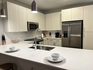 Eine moderne Küche mit weißer Arbeitsplatte, Edelstahlgeräten und hellen Holzschränken.