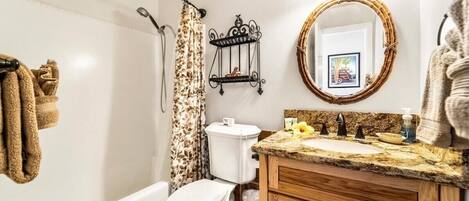 A bathroom with a toilet, sink, and shower. There is a towel rack with towels, a mirror, and a decorative wall piece.