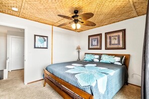 A bedroom with a wooden bed, a ceiling fan, and framed pictures on the wall. - Walk to Charming Kailua Village. Kailua Bay View. Lanai. AC. King Bed. Pool. (Kailua-Kona)