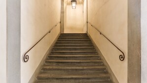 A staircase with a handrail, a light fixture at the top, and a plain wall.