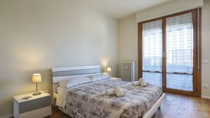 Et soveværelse med en seng, sengeborde med lamper, en radiator og udsigt gennem en glasdør.