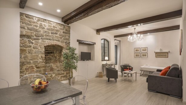 A modern living room with a stone wall, a dining area with a fruit bowl, and a grey sofa. - Florence Little Suite - Sweet Dreams in Florence (Firenze)