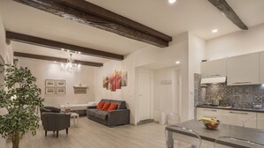 A modern living room with a sofa, dining table, and chairs, a kitchen with a tiled backsplash, and a chandelier. - Florence Little Suite - Sweet Dreams in Florence (Firenze)