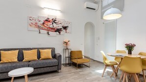 A modern living room with a gray sofa, yellow cushions, a round coffee table, and a dining area with yellow chairs and a white table. - Serenity - Sweet Dreams in Florence (Firenze)