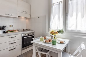 Une cuisine moderne avec des meubles blancs, un four encastré et une table à manger dressée avec de la nourriture et des boissons.