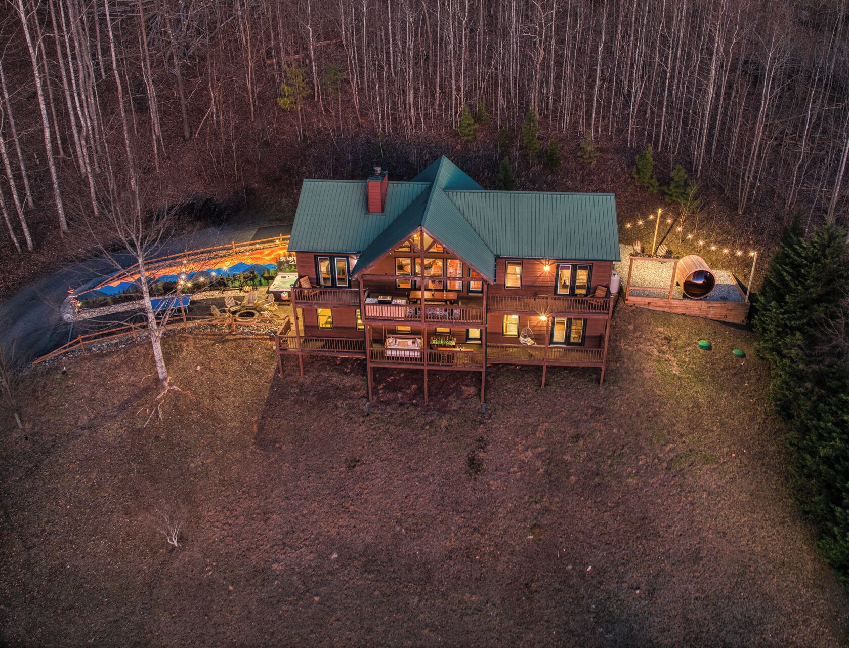 A two-story wooden cabin with a green roof, surrounded by a forest.