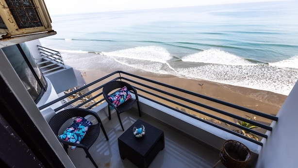 Un balcon avec deux fauteuils en osier, une petite table et une vue sur la plage et l’océan.
