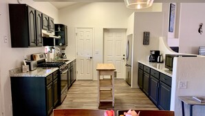 A modern kitchen with dark cabinets, a central island, and a dining area with a wooden table and chairs.