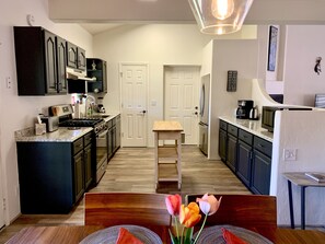 Une cuisine moderne avec des meubles de couleur sombre, un îlot central et un coin repas comprenant une table et des chaises en bois.