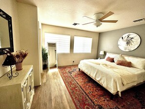 Un dormitorio con una cama grande, un ventilador de techo, una ventana y un espejo.