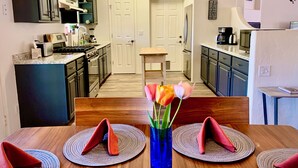 A modern kitchen with dark cabinets, a central island, and a dining area with a wooden table and red napkins.