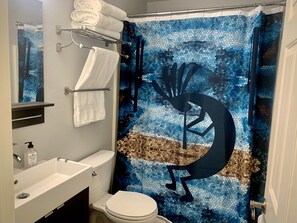 Un baño con lavabo blanco, inodoro y cortina de ducha con diseño de mosaico.