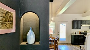 A modern kitchen with dark cabinets, a dining area with a wooden table and chairs, and a large white vase on a pedestal.