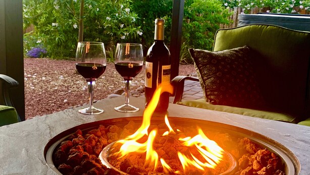 A fire pit table with two glasses of red wine and a bottle of wine.