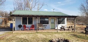 Une petite cabane dotée d’un porche abrité, de deux chaises Adirondack rouges, d’un barbecue et d’une table de pique-nique.