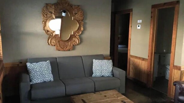 Un soggiorno con un divano grigio, cuscini decorati, un tavolino in legno e un grande specchio appeso al muro.