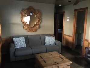 A living area with a grey sofa, patterned cushions, a wooden coffee table, and a large mirror on the wall. - Cabin #2 at Snug Harbor Cabins Lake Eufaula, OK (Stigler)