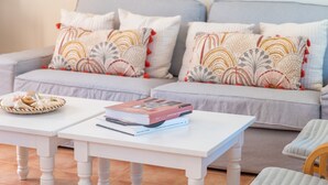 Una sala de estar con un sofá gris, cojines blancos, una mesa de centro blanca y una cesta de pan.