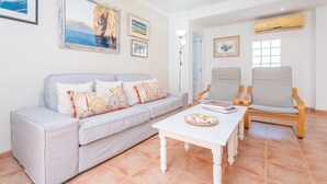 Una sala de estar con sofá, dos sillones, una mesa de centro y un aire acondicionado instalado en la pared.