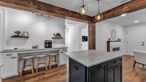 A modern kitchen with a central island, bar stools, wooden beams, and a fireplace. - Modern Boho Retreat with Piano. Fenced and Gated in Central Florida! (Lakeland)