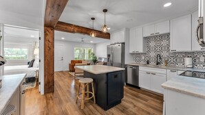 A modern kitchen with a central island, wooden beams, and a patterned backsplash. - Modern Boho Retreat with Piano. Fenced and Gated in Central Florida! (Lakeland)