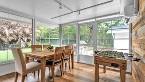 A bright room with large windows, a wooden table, chairs, and a foosball table. - Modern Boho Retreat with Piano. Fenced and Gated in Central Florida! (Lakeland)