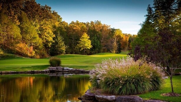 Ein friedlicher Golfplatz mit einem Teich, der die umliegenden Bäume spiegelt.