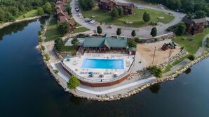 Luftaufnahme eines See-Resorts mit einem zentralen Schwimmbad, einer überdachten Terrasse und umliegenden Gebäuden.