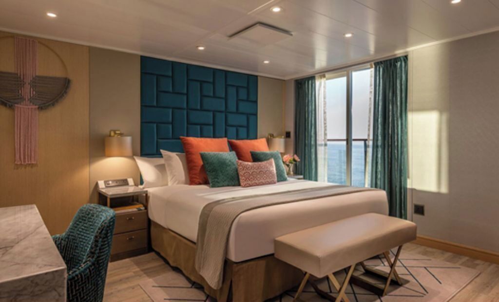 A modern hotel room with a large bed, a desk, and a view of the sea.