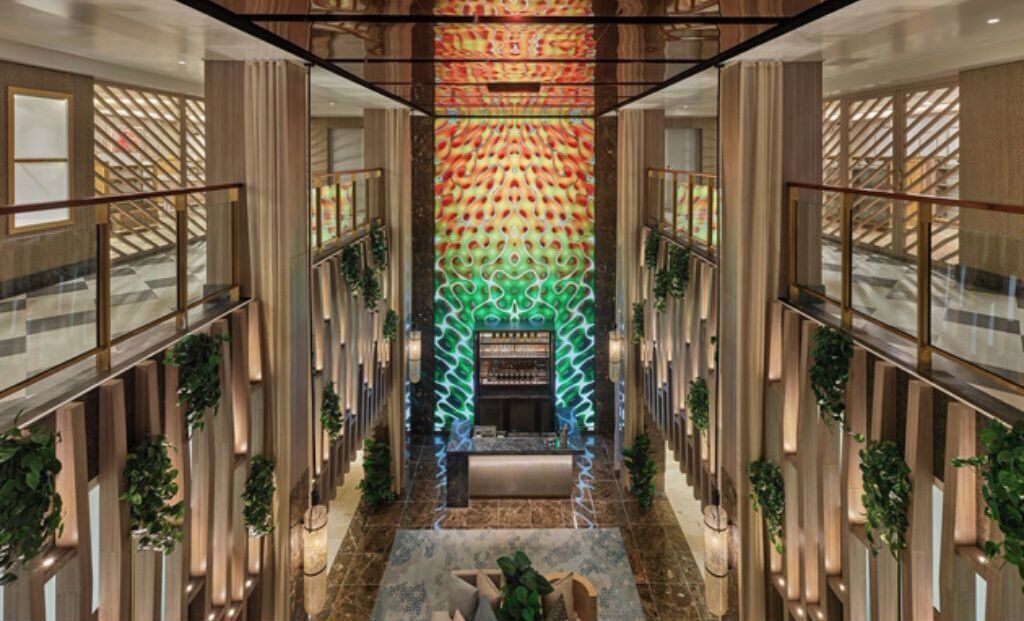 A modern hotel lobby with a central reception desk, high ceilings, and a patterned wall design.