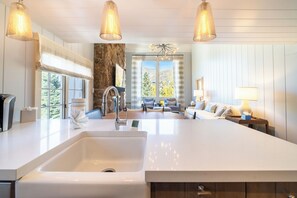 A modern kitchen with a large island, a stone accent wall, and a view of the outdoors. - Deluxe Snow-capped Suite, MTN views, hot tub+sauna access, steps from Vail Lifts (Vail)