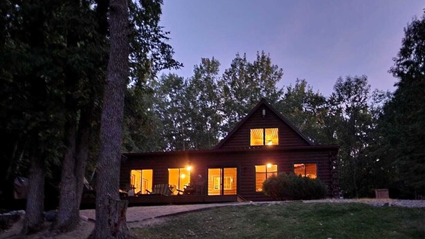 A two-story wooden cabin with multiple windows, surrounded by trees and a grassy yard.