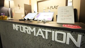 A reception desk with two laptops, a signboard with text, and a wall with a play symbol. - Bucheon THE Play (Bucheon)