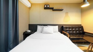 A hotel room with a bed, a chair, a desk, and a shelf with a sign. - Bucheon THE Play (Bucheon)