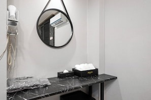 Une salle de bain équipée d’un sèche-cheveux, d’un miroir, d’un porte-serviettes et d’un boîte à mouchoirs.