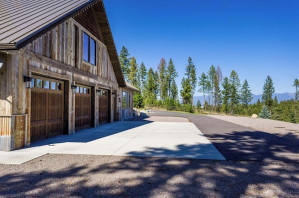 Un grand bâtiment en bois doté de plusieurs portes de garage, d’une allée pavée et surplombant un paysage montagneux.
