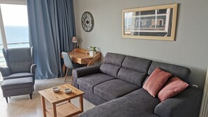 A modern living room with a grey sofa, a wooden coffee table, a grey armchair, and a dining table with chairs. - Valeria Sea View Apartment in Rethymno, Crete (Rethymno)