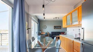 A modern kitchen with a glass dining table, wooden cabinets, and a stainless steel refrigerator. - Valeria Sea View Apartment in Rethymno, Crete (Rethymno)