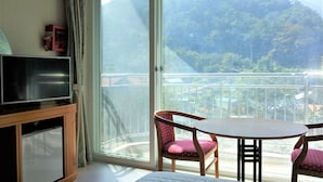 Une pièce avec un téléviseur posé sur un meuble, une table avec des chaises et un balcon offrant une vue sur les montagnes.