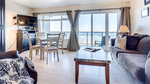 Amplia sala de estar con un gran ventanal con vista a la playa, un ventilador de techo y un comedor con sillas y una mesa.