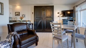 Una sala moderna con un sofá de cuero oscuro, una mesa de comedor con sillas, una zona de cocina con un mueble oscuro y un ventilador de techo.