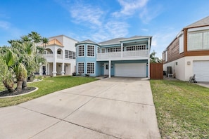 A two-story house with a garage, a covered driveway, and a well-maintained lawn. - Island Retreat w/ Heated Pool, Spa, BBQ & Games! (South Padre Island)