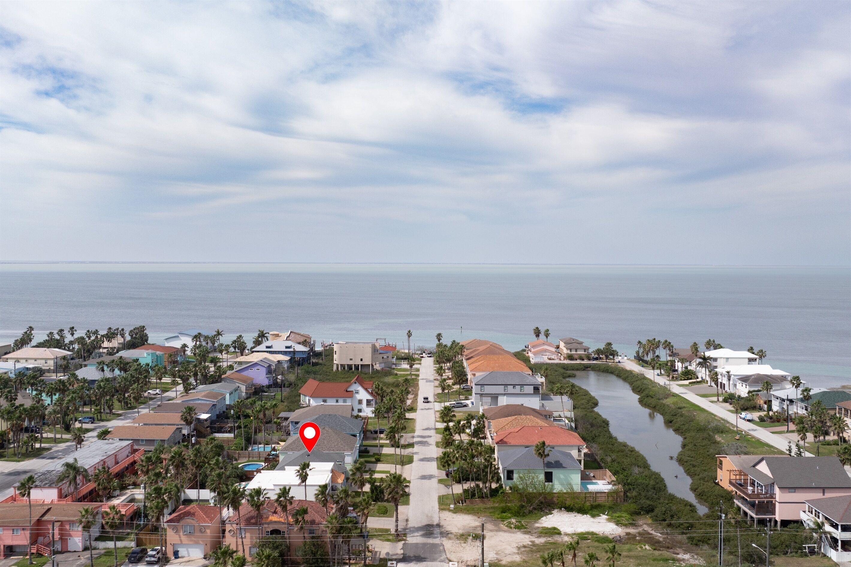 Vista aérea de una zona residencial costera con casas, un canal estrecho y una playa al fondo.