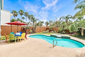 A swimming pool with a curved edge, surrounded by palm trees and a wooden fence. - Island Retreat w/ Heated Pool, Spa, BBQ & Games! (South Padre Island)