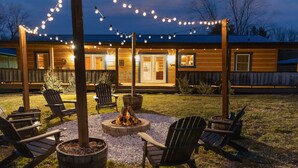 Un espace extérieur accueillant, aménagé avec des fauteuils Adirondack, un foyer et des guirlandes lumineuses.