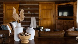 L'intérieur d'un chalet en bois, avec un canapé, deux vases blancs ornés de plumes d'herbe des pampas et un bol en bois contenant des objets décoratifs.