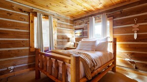 Une chambre à coucher dans un chalet en bois, avec un lit, des rideaux, une table de chevet et un téléviseur fixé au mur.