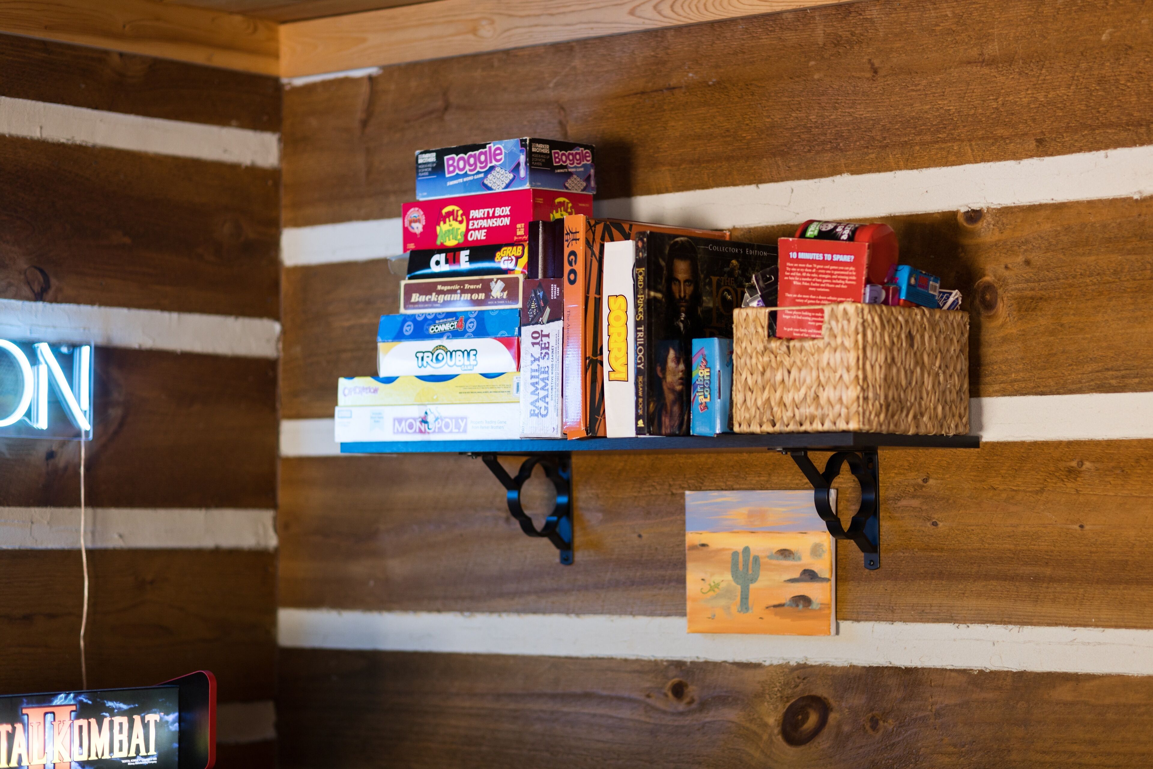 Un mur en bois avec une étagère où sont rangés des jeux de société et un panneau lumineux au néon.
